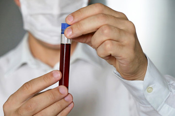 Test tube in male hands close up, man in medical mask holding a vial with red liquid. Concept of blood sample, medical and chemical research, vaccination, doctor or scientist