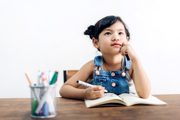 School kid little girl learning and writing in notebook with pencil making homework at...