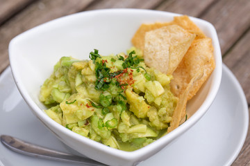 Avocado guacamole with tortilla chips in a white bowl. Green guacamole and dipping tortilla chips