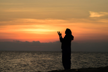 Muslim Girl saying prayer by the beach with sunset