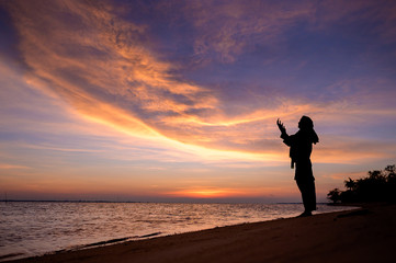 Fototapeta premium Muslim Girl saying prayer by the beach with sunset