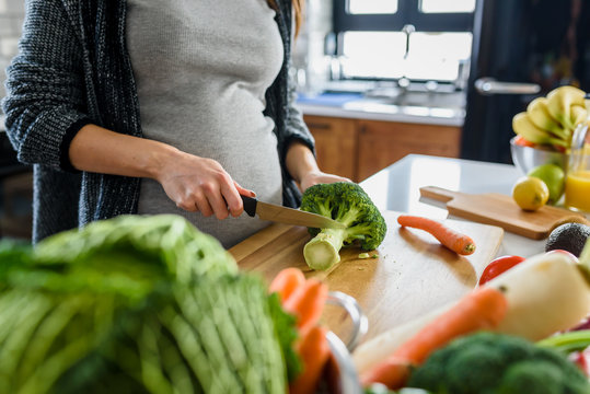 Young pregnant woman preparing healthy food with lots of vegetables at home kitchen