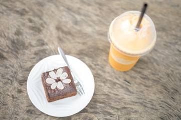 Chocolate cake, brownie fudge on white plate and a glass of milk tea frappe with wooden background