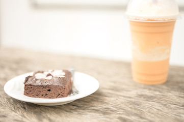 Chocolate cake, brownie fudge on white plate and a glass of milk tea frappe with wooden background