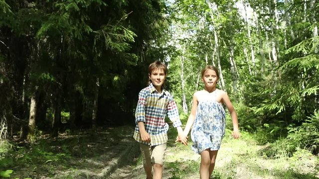 Girl and boy run forward holding hands in a road in the woods. Childhood. Kids, nature, summer casual fashion.