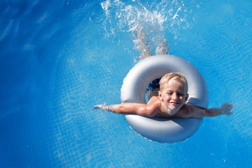 A blond-haired boy swims in a blue water pool on a beautiful sunny day