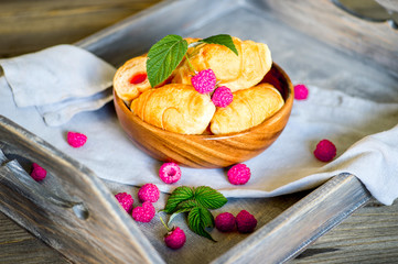 Croissants with raspberries on a wooden tray. The concept of a wholesome breakfast.