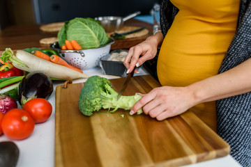 Young pregnant woman preparing healthy food with lots of vegetables at home kitchen