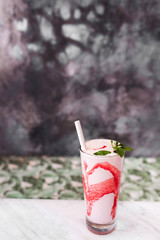 Fresh tasty cold milk shake with red strawberry syrup on white marble table. Gray concrete background. Sweet frappuccino beverage. Summer drink concept.
