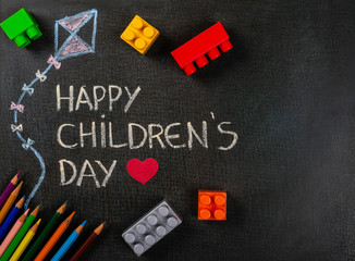 Fototapeta na wymiar Blackboard written Happy Children's Day and kite drawing with scattered assembly pieces and color pencils. Copy space.