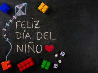 Blackboard written feliz dia del niño (spanish). Kite design with assembling pieces and game dice. Copy space..