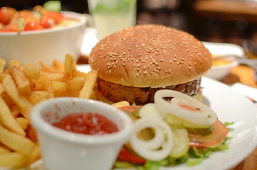 Hamburger, french fries, ketchup, and fresh vegetables salad served at restaurant