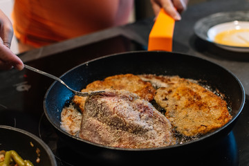 turning over a piece of breaded pork in the pan for dinner