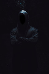 A beefy man in a black robe and hood stands with his arms folded on his chest on a black isolated...