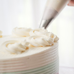 Fototapeta na wymiar Confectioner topping cakes with cream using a pastry bag,