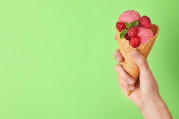 Woman holding wafer cone with delicious raspberry ice cream on green background, closeup. Space for text