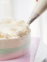 Confectioner topping cakes with cream using a pastry bag,