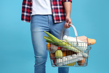 Man with shopping basket full of products on blue background, closeup