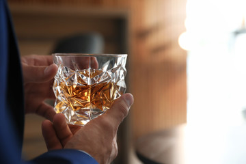 Young man with glass of whiskey indoors, closeup view. Space for text