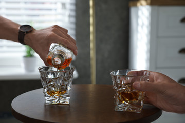 Young men drinking whiskey together at home, closeup