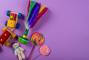 Children's Day. Wooden train, shuttlecock, teddy bear, lollipops on purple neon background. Copy space, graphic resource.