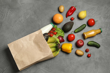 Paper bag with groceries on grey background, flat lay
