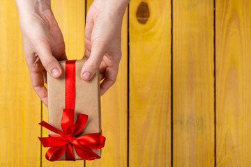 Children's Day. Female hand delivering gift with red bow on yellow background. Copy space, graphic resource.
