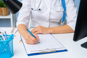 Woman doctor taking notes on clipboard while sitting at her table in office