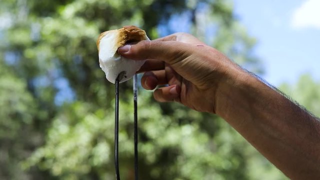 Slow motion shot of someone pulling a gooey golden brown marshmallow off of a metal skewer to make S'mores.