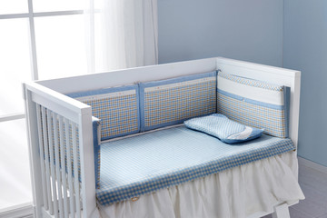 Children's bed in an empty room, lit by sunlight. There are checked mats and pillows on the bed