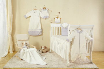 There are baby clothes, cribs, sheets, pillows and sleeping bags in the nursery.