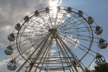White Ferris wheel against a Sunny summer sky with white clouds.