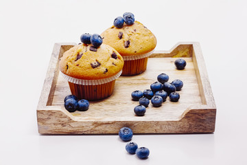 Muffins and bluebeeries on wooden tray over white background
