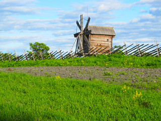Wooden mill of the last century at the fence of the poles in the summer..
