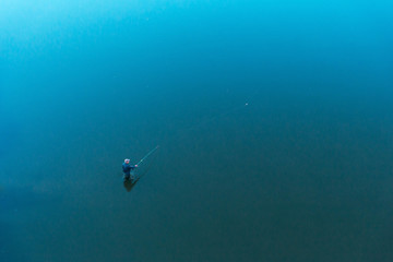 Fototapeta premium a lone fisherman standing in the water throws tackle. float rod. the view from the top. the shores cannot be seen.