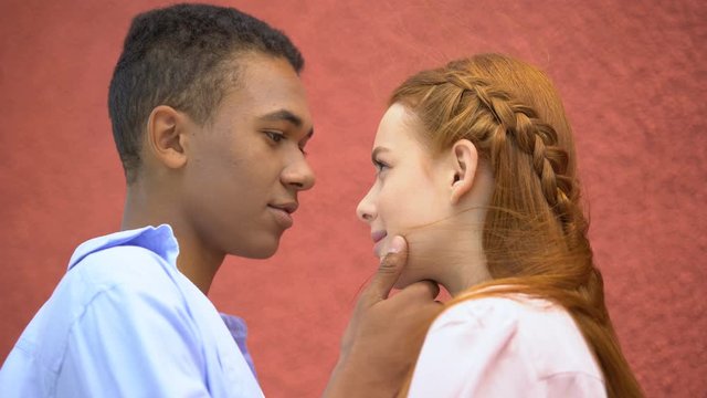 Mixed-race boyfriend tenderly holding girlfriends chin, moment of first kiss