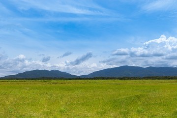 Landscape of sunny green grass field and mountain under the summer blue sky.