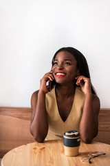 Smiling black girl talking by smartphone at cafe.