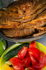 Lot of fried crisp fish on iron dish on the table served with pieces of vegetables. Closeup. Summer picnic. Outdoors