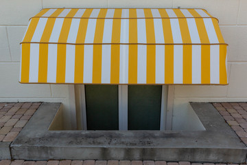 Canopy over the basement window with white and yellow stripes near the stone pavement.