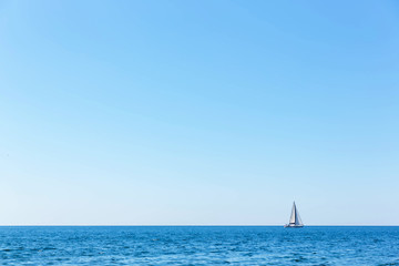A single sailboat under white sails floats in the sea against the blue sky.