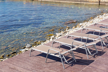 Wicker beds with a metal base are on a brown, wooden flooring near the sea.