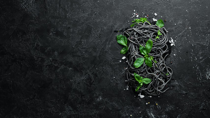 Black pasta with basil. On a black stone background. Top view. Free copy space.