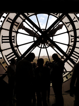 Silhouettes of tourists visiting d'Orsay Museum shot against big external clock