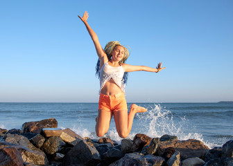 Senegalese girl with pigtails jumps on the wooden jetty on the sea. The waves are hitting the rocks and the spray is flying in different directions. Vacation.