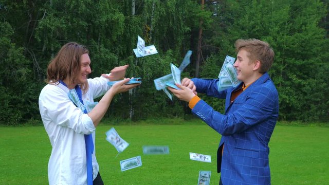 Two young man throw money (100 dollar bill) into the air in a park in nature.