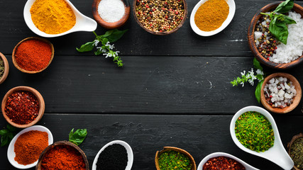 Large spice and herb collection in bowls and spoons. Indian spices. On a black wooden background. Top view.