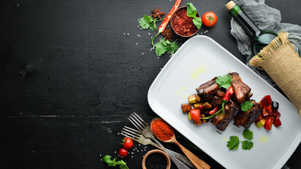 Baked pork ribs with vegetables. In the plate. On a wooden background. Top view. Free space for your text.