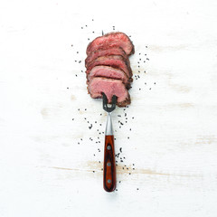 Beef steak on a fork. On a wooden background. Top view. Free space for your text.