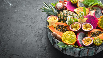 Tropical fruits: papaya, mangosteen, cactus fruit, pytahaya, pineapple on a black background. Top view. Free space for text.